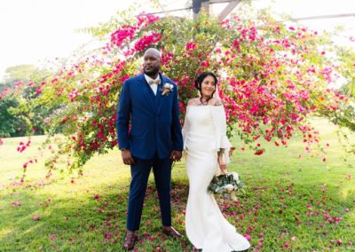 Bride and groom in a navy suit posing before a cascade of pink bougainvillea