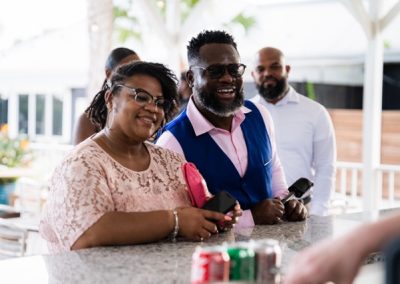 Two smiling guests at the outdoor bar, one in a pink shirt and blue vest