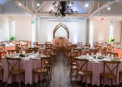 Reception hall set with pink-linen round tables, crossback chairs and a wrought-iron chandelier