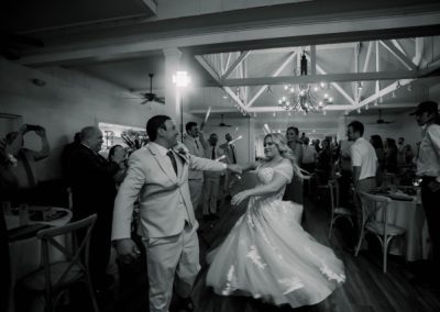 Groom twirling the bride on the dance floor as guests cheer, in black and white