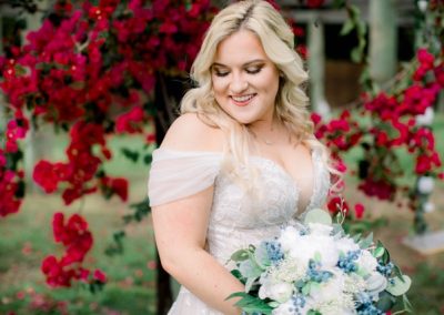 Bride smiling down at her blue-and-white bouquet with red bougainvillea behind her