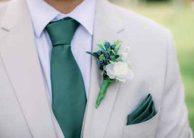 Close-up of a groom's white suit with green tie and white berry boutonniere