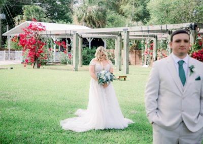 First look on the lawn as the bride approaches the groom near a bougainvillea pergola