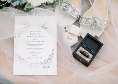 Wedding invitation for Kaylee and Fabio beside a ring box and beaded shoes on soft tulle