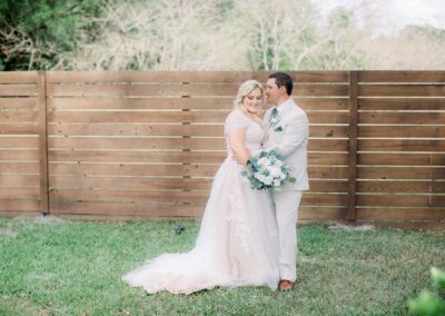 Bride and groom embracing along a horizontal wood fence with a blue-and-white bouquet