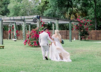 Bride and groom walking across the lawn toward a rose-covered pergola