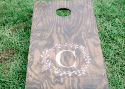 Wood cornhole board with a monogrammed C resting on the lawn