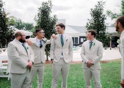 Groomsmen in tan suits with green ties laughing together on the lawn