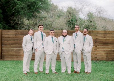 Groomsmen in tan suits with green ties posing along a wooden fence