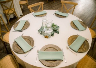 Round reception table set with sage napkins, woven chargers and a eucalyptus centerpiece