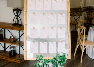 Gold-framed mirror seating chart with escort cards and a greenery stand
