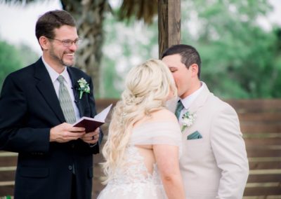 Groom kissing his bride's forehead at the altar as the smiling officiant reads