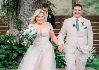 Bride and groom walk hand in hand from their ceremony beneath a floral arch