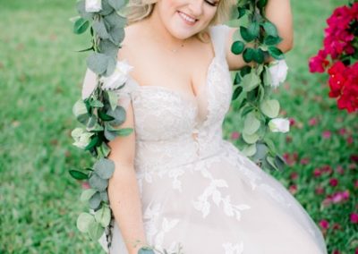 Bride seated on a greenery-wrapped swing holding a blue and white bouquet