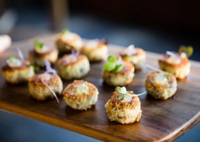 Bite-sized crab cakes topped with microgreens on a wooden serving plank