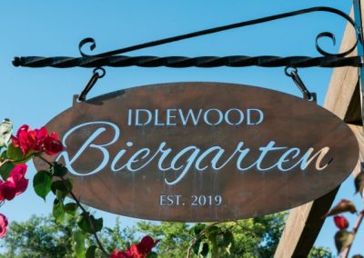Idlewood Biergarten sign framed by pink bougainvillea blossoms