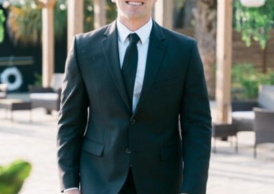 Groom in a black suit smiling as he walks through the garden patio