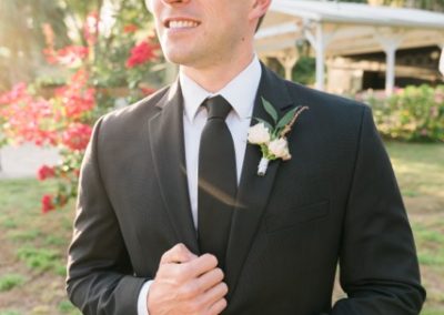 Groom in a black suit in the garden lit by warm golden afternoon light