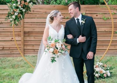 Bride and groom smiling at each other before a round gold floral ceremony arch