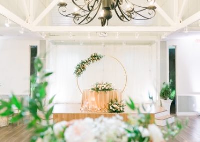 Iron chandelier above a draped sweetheart table and floral arch, roses in foreground