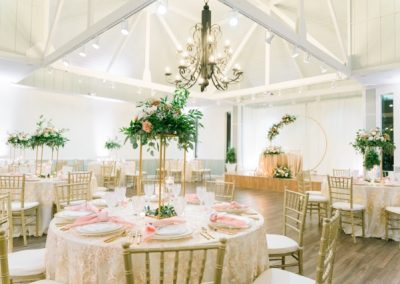 Reception hall with round tables, gold chiavari chairs and tall greenery centerpieces