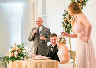 Guest gives a toast as the seated newlyweds laugh at their sweetheart table