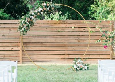 Round gold floral ceremony arch on the lawn before a wooden privacy fence